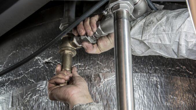 VVS-montørs hænder samler en rørinstallation med messingfittings bag en isoleret væg